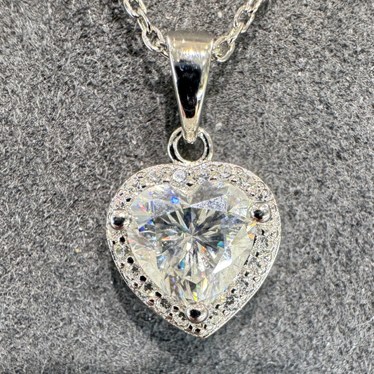 Heart-shaped silver pendant with clear gemstone on a textured surface
