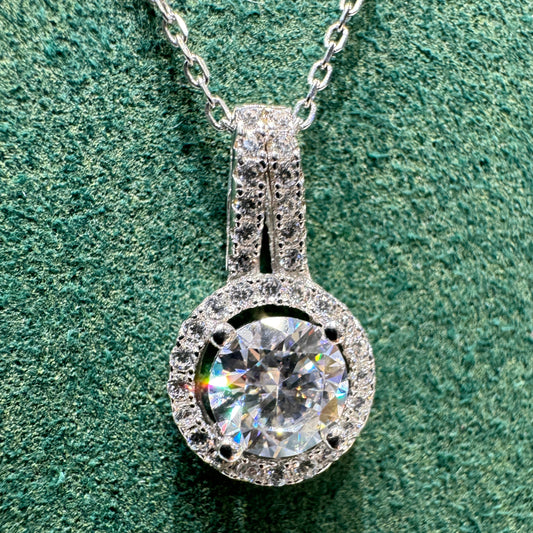 Silver necklace with a large diamond pendant on a green textured surface