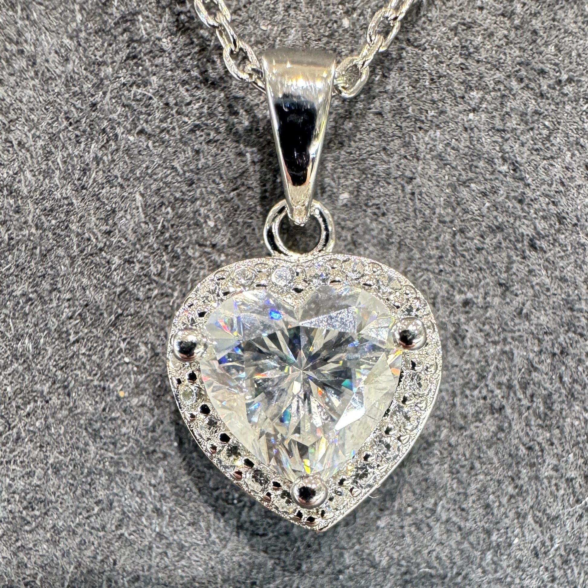 Heart-shaped silver pendant with clear gemstone on a textured surface