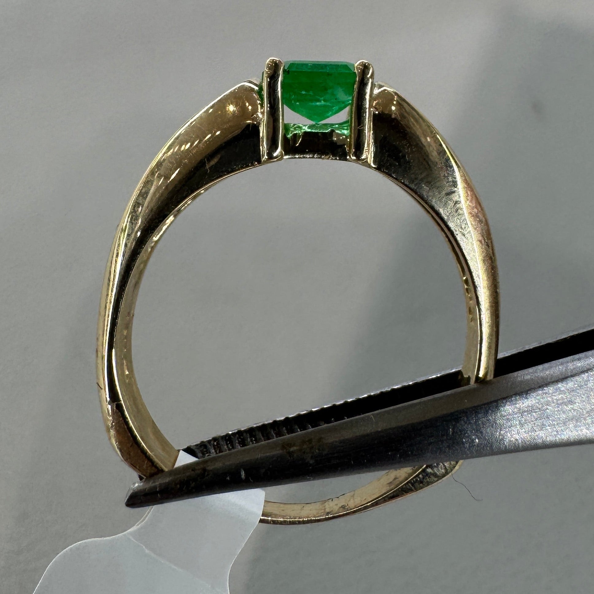 Gold ring with a green gemstone held by scissors on a gray background