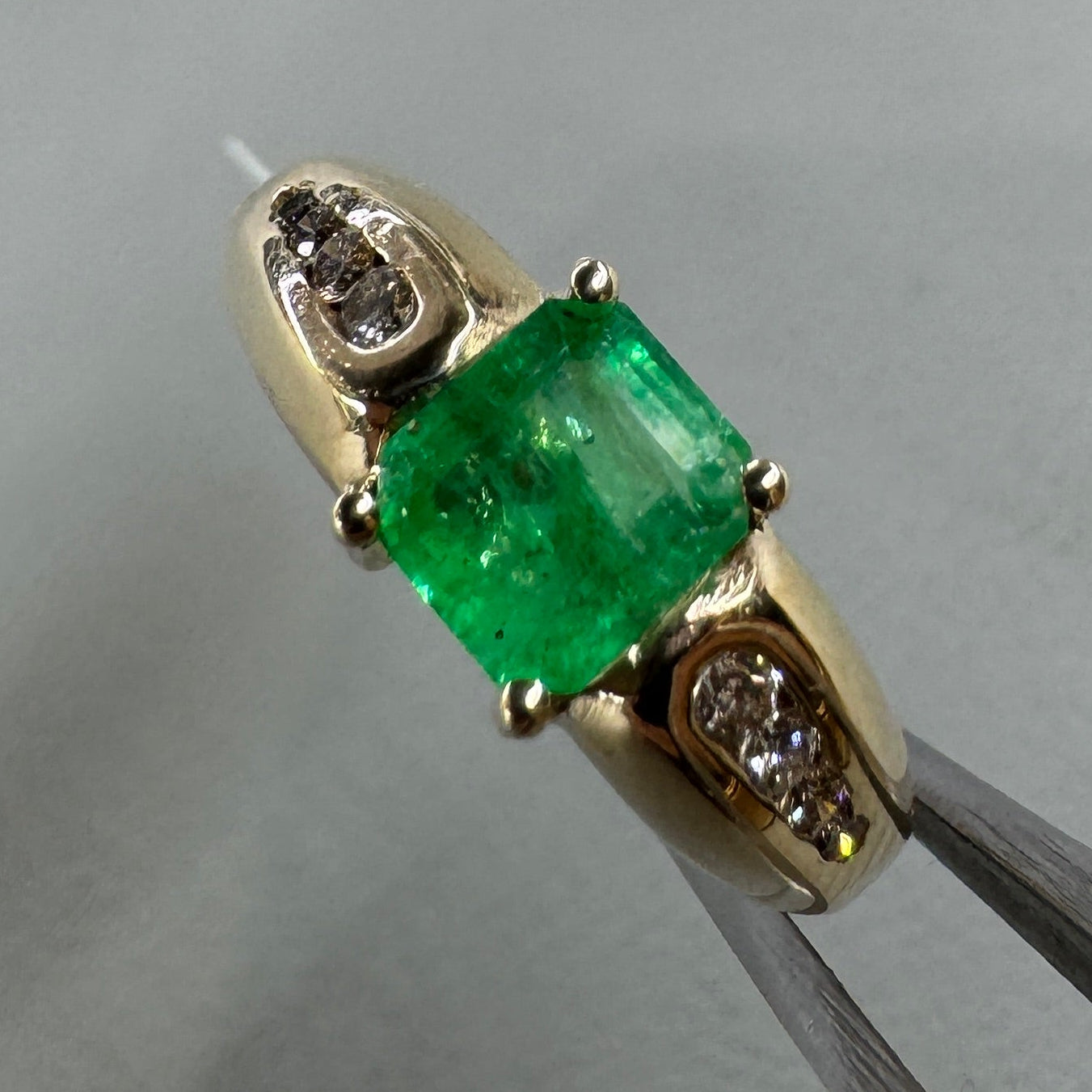Gold ring with a green gemstone held by tweezers on a light gray background